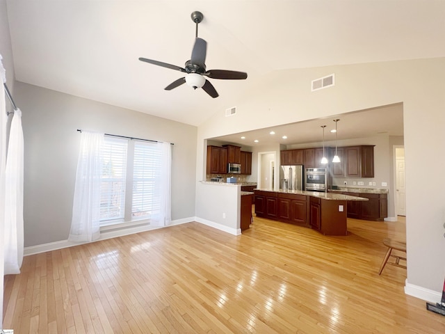 kitchen with lofted ceiling, hanging light fixtures, a kitchen island, appliances with stainless steel finishes, and light hardwood / wood-style floors