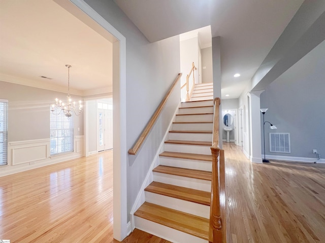 stairs featuring a chandelier, wood-type flooring, and crown molding