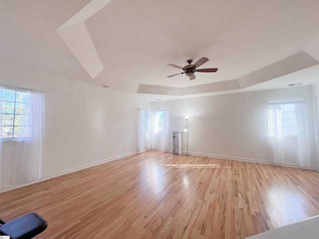 empty room featuring a tray ceiling, light hardwood / wood-style flooring, plenty of natural light, and ceiling fan