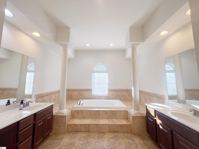 bathroom featuring vanity, a relaxing tiled tub, tile walls, and decorative columns