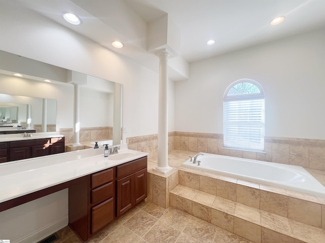 bathroom featuring ornate columns, vanity, and a relaxing tiled tub