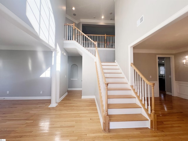 stairway featuring a towering ceiling, hardwood / wood-style flooring, decorative columns, and ornamental molding