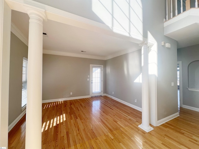 interior space featuring ornate columns, crown molding, a towering ceiling, and hardwood / wood-style flooring