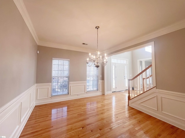 unfurnished dining area with ornamental molding, light wood-type flooring, and a notable chandelier