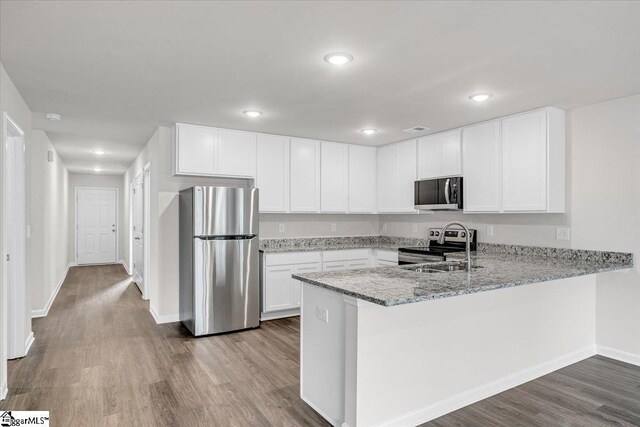 kitchen with sink, stainless steel appliances, wood-type flooring, white cabinets, and kitchen peninsula