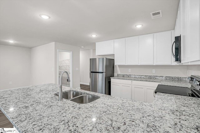 kitchen with stainless steel refrigerator, sink, white cabinets, stove, and light stone counters