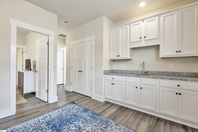 kitchen with white cabinets, wood-type flooring, light stone counters, and sink