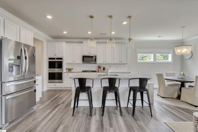 kitchen with light stone countertops, appliances with stainless steel finishes, a kitchen island with sink, white cabinets, and hanging light fixtures