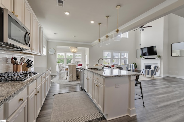 kitchen with pendant lighting, white cabinets, ceiling fan with notable chandelier, a center island with sink, and stainless steel appliances