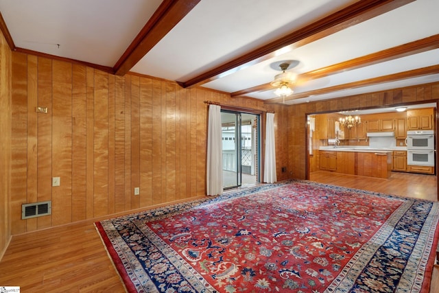 living room with beamed ceiling, ceiling fan with notable chandelier, light hardwood / wood-style floors, and wooden walls