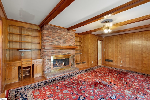 unfurnished living room featuring a brick fireplace, beamed ceiling, wood walls, crown molding, and hardwood / wood-style floors