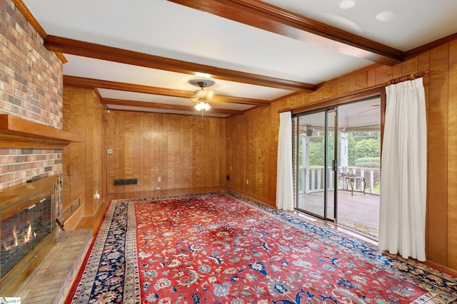 unfurnished living room featuring wooden walls, a fireplace, beamed ceiling, and ceiling fan