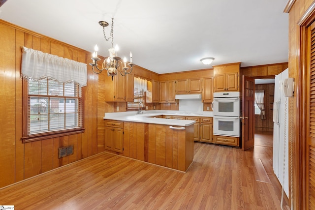 kitchen with white double oven, sink, hanging light fixtures, kitchen peninsula, and a chandelier