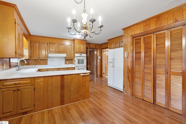 kitchen featuring kitchen peninsula, white appliances, sink, pendant lighting, and a chandelier