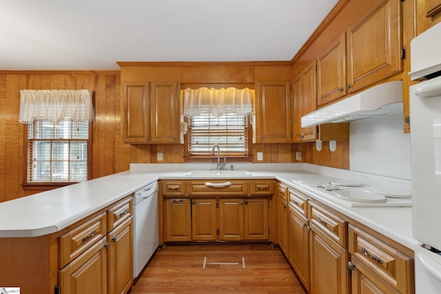 kitchen featuring sink, kitchen peninsula, white appliances, wooden walls, and light wood-type flooring