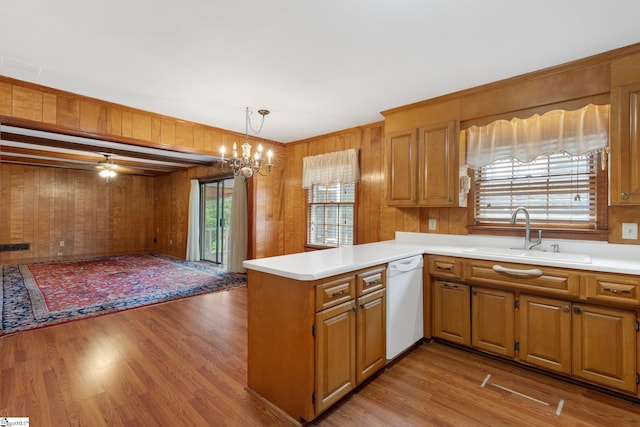 kitchen with sink, dishwasher, kitchen peninsula, wood walls, and pendant lighting