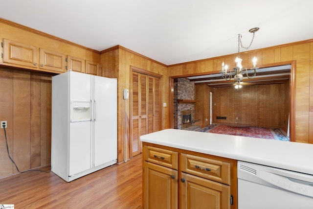 kitchen featuring white appliances, wooden walls, a fireplace, decorative light fixtures, and a chandelier