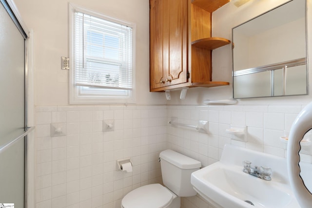 bathroom featuring toilet, a shower with door, sink, and tile walls