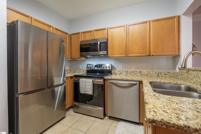 kitchen featuring light stone countertops, appliances with stainless steel finishes, light tile patterned floors, and sink