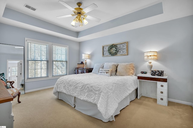 carpeted bedroom with a raised ceiling and ceiling fan