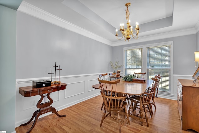 dining room with a notable chandelier, light hardwood / wood-style floors, a raised ceiling, and crown molding