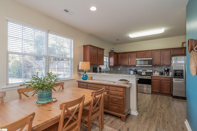 kitchen with appliances with stainless steel finishes, backsplash, hardwood / wood-style flooring, and a healthy amount of sunlight