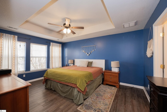 bedroom with ceiling fan, dark hardwood / wood-style floors, and a raised ceiling