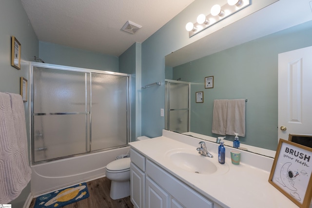 full bathroom with vanity, combined bath / shower with glass door, hardwood / wood-style flooring, toilet, and a textured ceiling