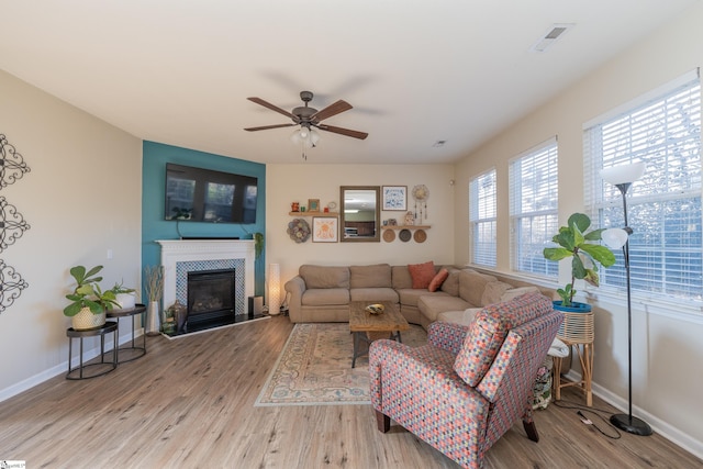 living room with ceiling fan, light wood-type flooring, and a tile fireplace