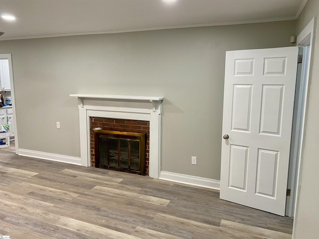 unfurnished living room with wood-type flooring, crown molding, and a brick fireplace