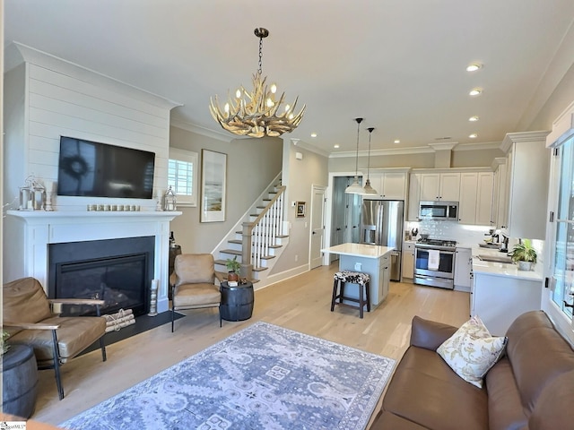 living room featuring ornamental molding, a large fireplace, light hardwood / wood-style floors, and an inviting chandelier