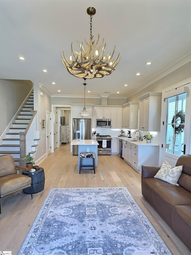 living room with light hardwood / wood-style floors, crown molding, sink, and an inviting chandelier