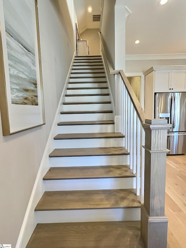 staircase with wood-type flooring and ornamental molding