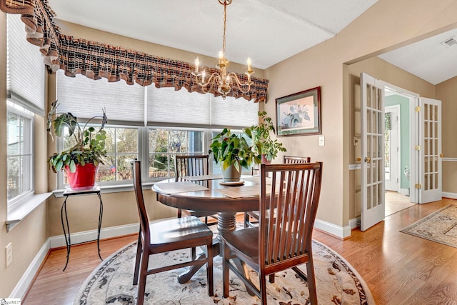 dining area with a textured ceiling, french doors, light hardwood / wood-style flooring, and an inviting chandelier