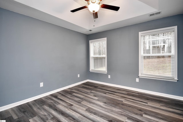 spare room with dark hardwood / wood-style flooring, a raised ceiling, plenty of natural light, and ceiling fan