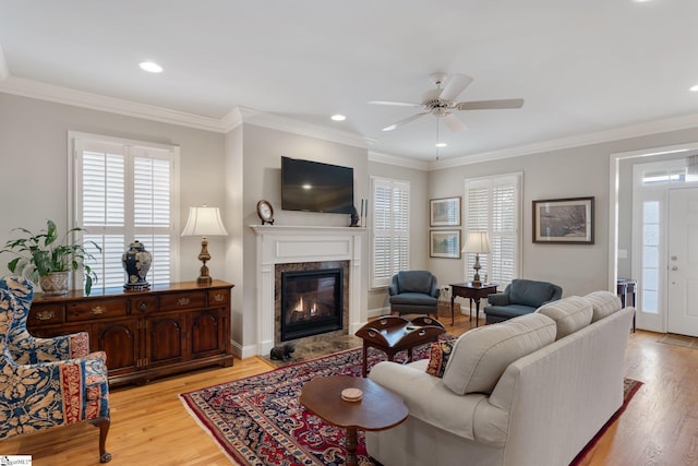 living room featuring a fireplace, light hardwood / wood-style floors, ceiling fan, and crown molding