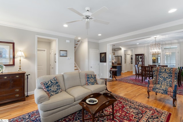 living room with ceiling fan with notable chandelier, light hardwood / wood-style floors, and ornamental molding