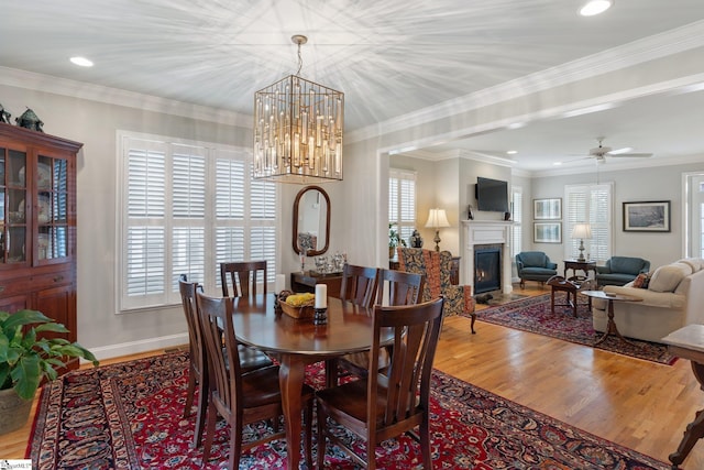 dining space with crown molding, plenty of natural light, wood-type flooring, and ceiling fan with notable chandelier