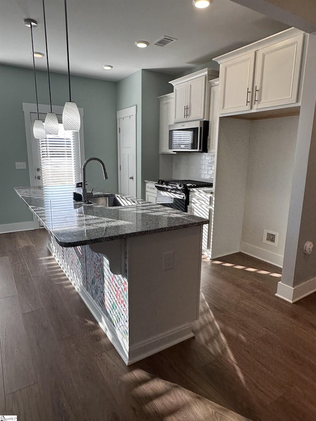 kitchen featuring pendant lighting, dark stone counters, an island with sink, appliances with stainless steel finishes, and white cabinetry