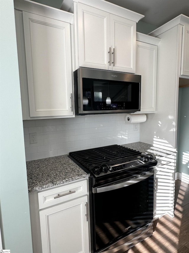 kitchen featuring hardwood / wood-style floors, black stove, decorative backsplash, light stone countertops, and white cabinetry