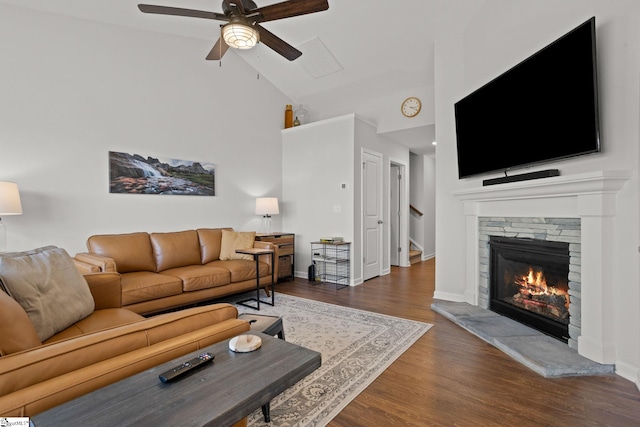 living room featuring dark hardwood / wood-style floors, ceiling fan, a stone fireplace, and high vaulted ceiling