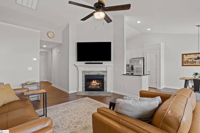 living room featuring hardwood / wood-style floors, ceiling fan, a stone fireplace, and vaulted ceiling