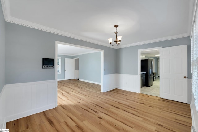 empty room featuring a notable chandelier, ornamental molding, and light hardwood / wood-style flooring