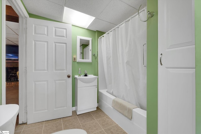 full bathroom featuring a drop ceiling, shower / bathtub combination with curtain, sink, tile patterned floors, and toilet