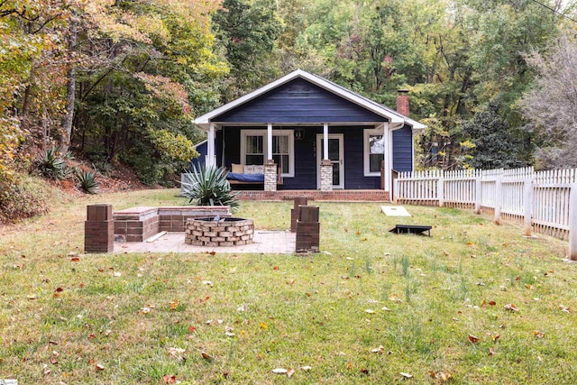 bungalow-style house with covered porch, a front lawn, and an outdoor fire pit