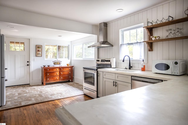 kitchen with stainless steel appliances, a wealth of natural light, wall chimney exhaust hood, and sink