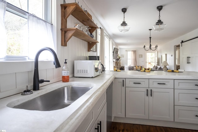 kitchen featuring dark wood-type flooring, white cabinets, sink, hanging light fixtures, and a barn door