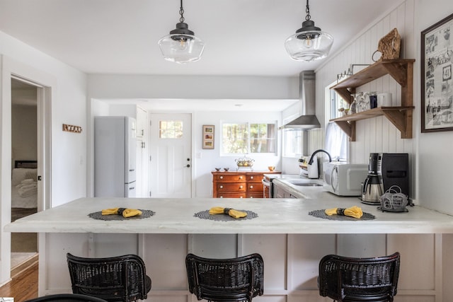 kitchen with pendant lighting, sink, wall chimney exhaust hood, kitchen peninsula, and a breakfast bar area