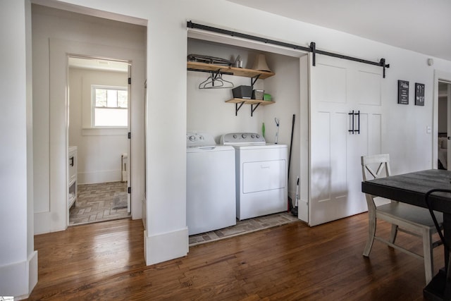 laundry area with a barn door, washing machine and dryer, and dark wood-type flooring