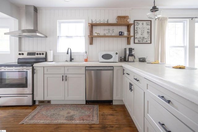 kitchen featuring sink, hanging light fixtures, stainless steel appliances, wall chimney range hood, and white cabinets